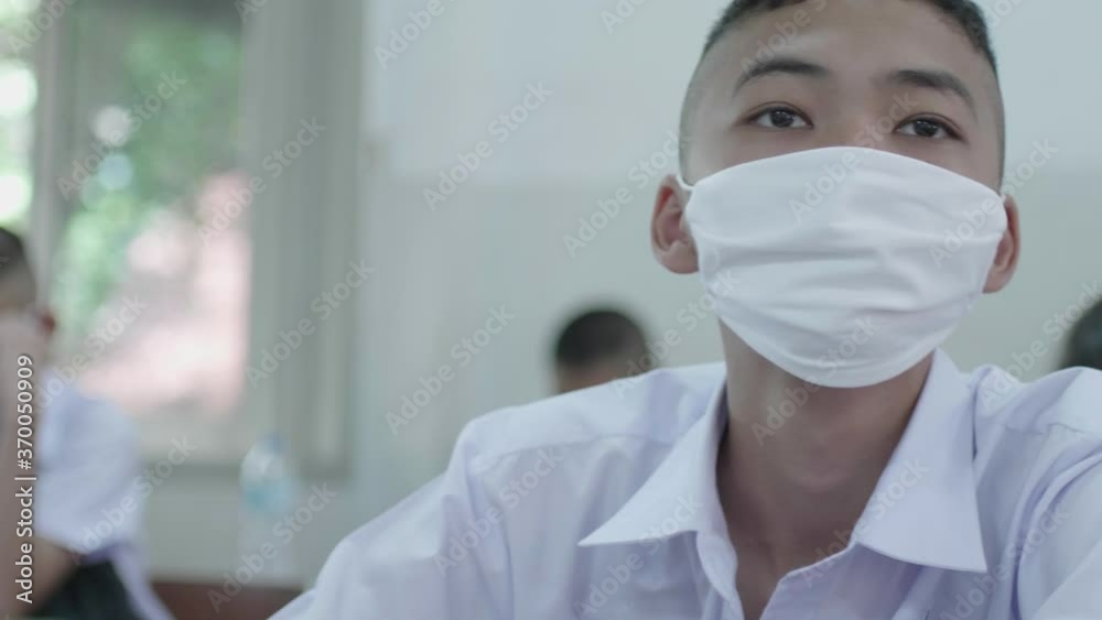 Slow motion of a male Asian high school student in white uniform and wearing a white mask is studying in classroom during the Coronavirus 2019 (Covid-19) epidemic. Slow motion of a male Asian high school student in white uniform and wearing a white mask is studying in classroom during the Coronavirus 2019 (Covid-19) epidemic.