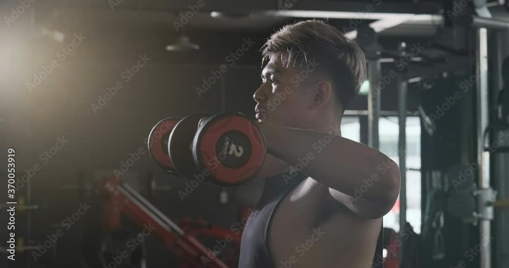 Sportsman doing warm-up exercises with dumbbell in the fitness gym. Sportsman doing warm-up exercises with dumbbell in the fitness gym.