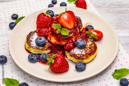 Cottage cheese pancakes with fresh berries and strawberry sauce. Healthy breakfast concept on wooden background