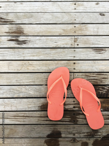 orange jandals or flip-flops on a wooden boardwalk near a swimming pool, top-down minimal detail photo photo