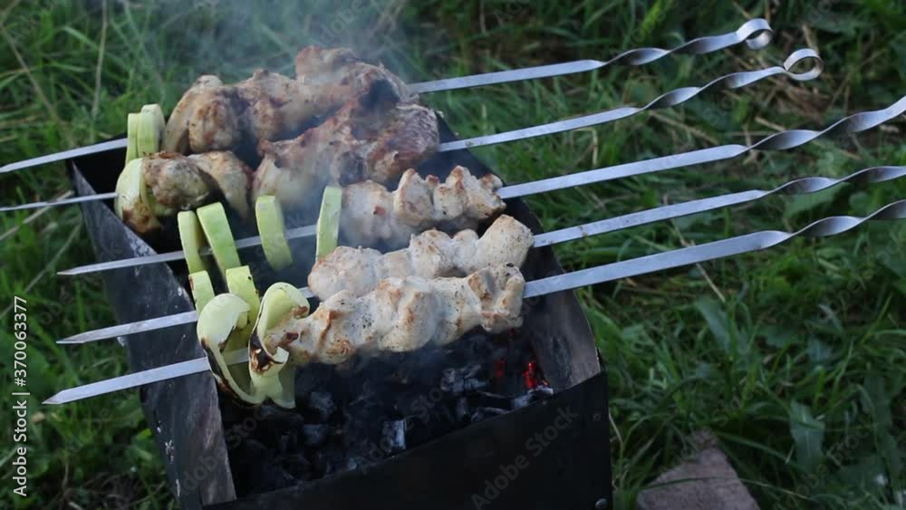 The shish kebab is cooked on the grill. The man blows air over the coals.