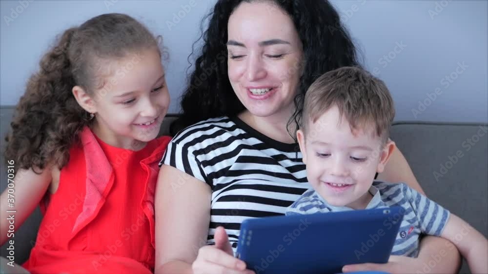 Happy family,mom and cute little children watch the phone,mom plays with children at home,relaxing using a smartphone,hugging,sitting on the couch, laughing, having fun,enjoying moments of family life Happy family,mom and cute little children watch the phone,mom plays with children at home,relaxing using a smartphone,hugging,sitting on the couch, laughing, having fun,enjoying moments of family life
