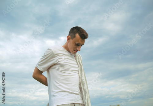 Handsome guy puts on a shirt against the background of the sky. Men's fashion, unity with nature.