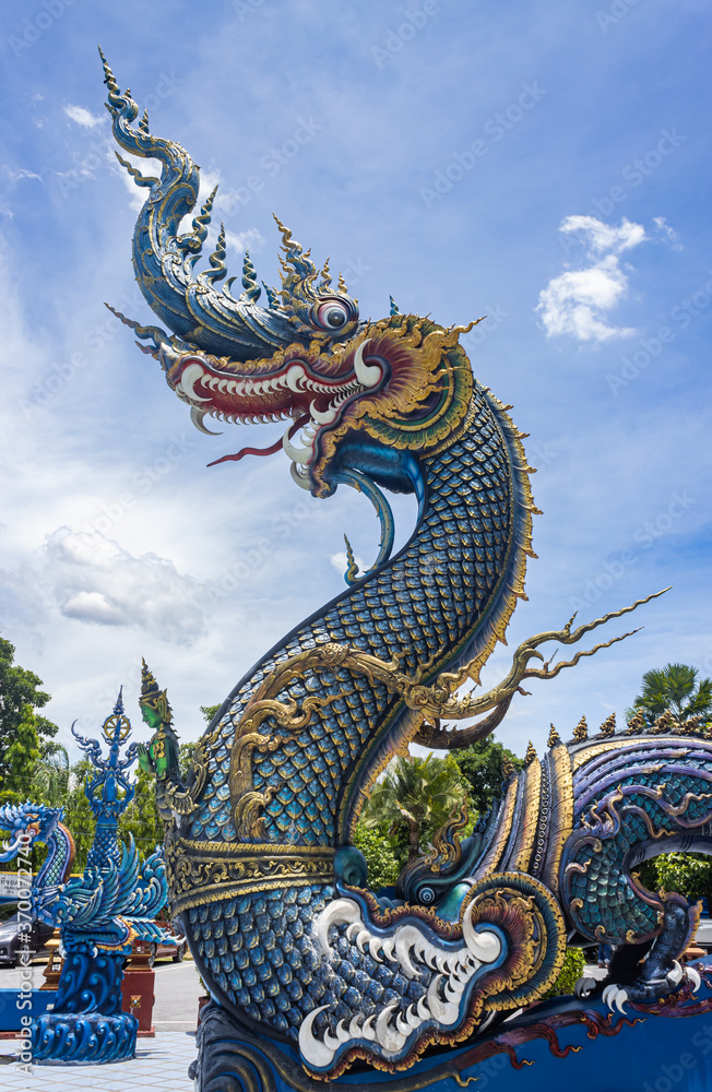 Fototapeta premium Chiangrai, Thailand - June 7, 2020: Blue Serpent or Naga on Blue Sky Background with Natural Light in Wat Rong Suea Ten Temple at Chiangrai Thailand in Portrait View