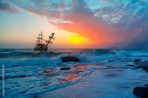 Old Sailing-ship in storm sea, dramatic sunset in the background