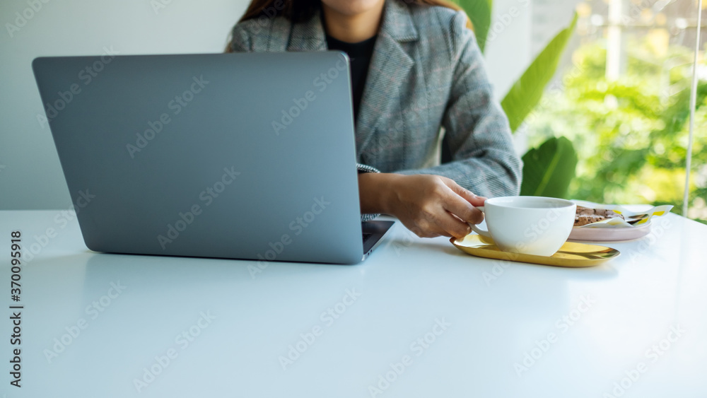 Closeup image of a business woman using and working on laptop computer while drinking coffee in office Closeup image of a business woman using and working on laptop computer while drinking coffee in office