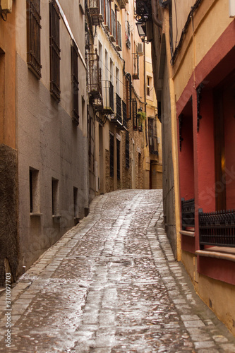 Fototapeta Naklejka Na Ścianę i Meble -  Cityscape. History and architecture. Colorful buildings with ancient design. View of the narrow alley and wet street after rain, in Toledo, Spain. 