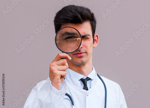 A doctor on a gray background holds a magnifying glass in a medical dressing gown, doctor, medicine.