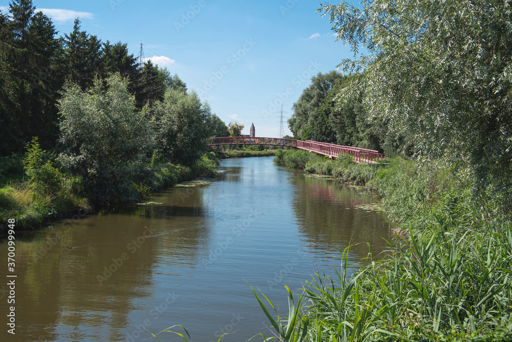 Lokeren, Belgium, Landscape photo with a river, a footbridge and a church tower in the distance Lokeren, Belgium, Landscape photo with a river, a footbridge and a church tower in the distance