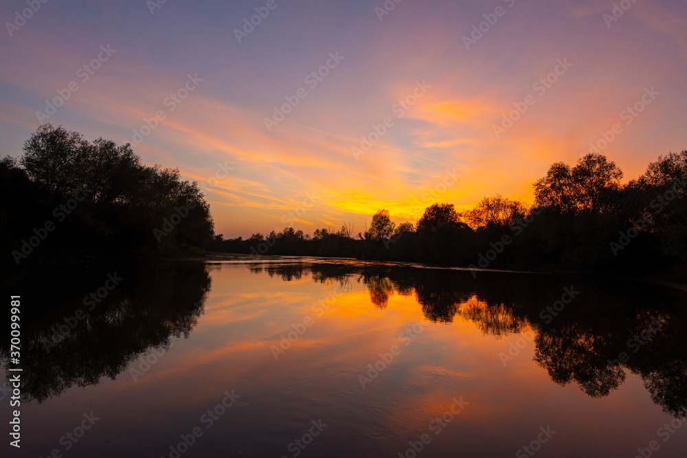 Wild, colorful sunset over tranquill river in a remote area in Europe