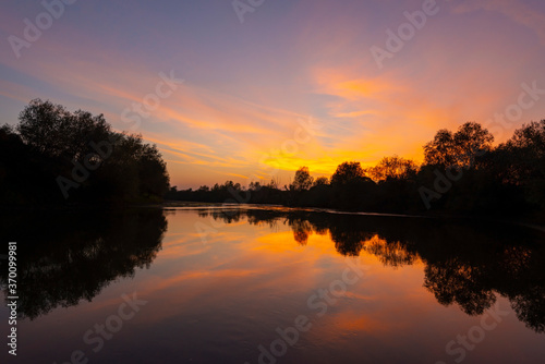 Wild, colorful sunset over tranquill river in a remote area in Europe