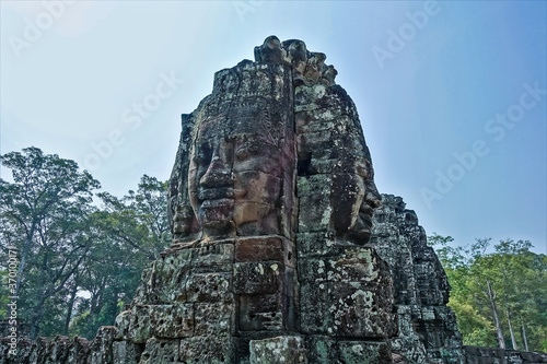 Strange statues at the top of the temple. In the clear sky, huge human faces look in different directions. There are mysterious smiles on their lips. Ancient stones are dilapidated. Cambodia. Angkor. © Вера 