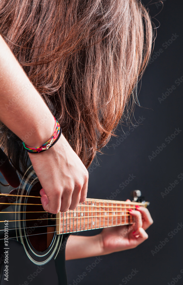 Fototapeta premium Portrait of young young beautiful girl with long hair playing an black acoustic guitar on black background 