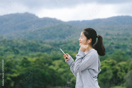 young asian woman enjoying and listening to music on her mobile phone in park. refreshing natural atmosphere.
