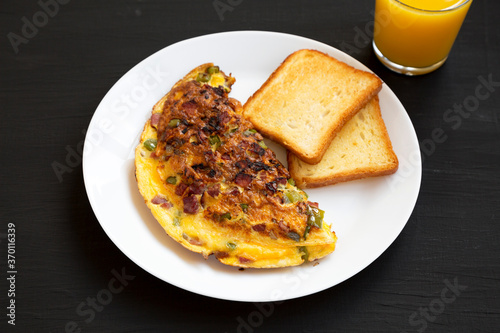 Homemade Denver Omelette on a white plate on a black background, low angle view.