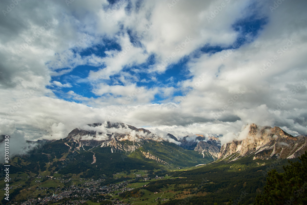 A panoramic landscape view of clouds over The Dolomites mountain ranges overlooking an alpine valley below. A scenic view taken from Monte Cristallo near Cortina in Italy.