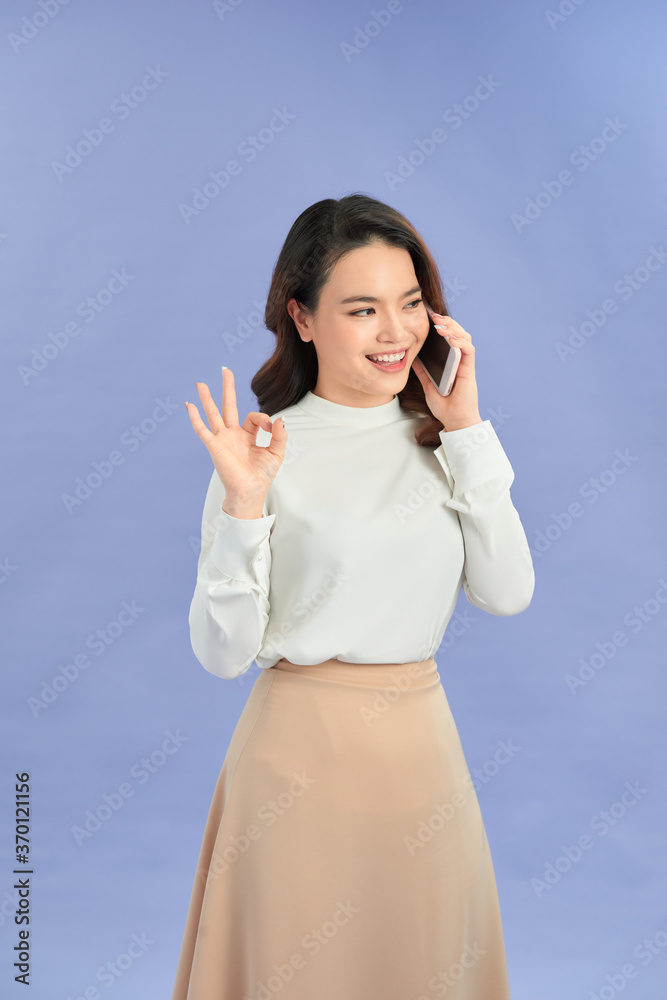 Young woman talking mobile over isolated purple background showing ok sign with fingers Young woman talking mobile over isolated purple background showing ok sign with fingers