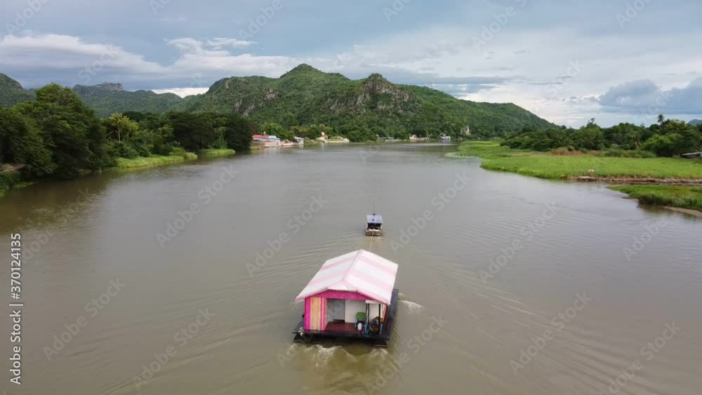 Aerial view of motor boat pulling raft house in river with mountain and sky view. landscape of floating hotel on river in Kanchanaburi, Thailand. Aerial view of motor boat pulling raft house in river with mountain and sky view. landscape of floating hotel on river in Kanchanaburi, Thailand.