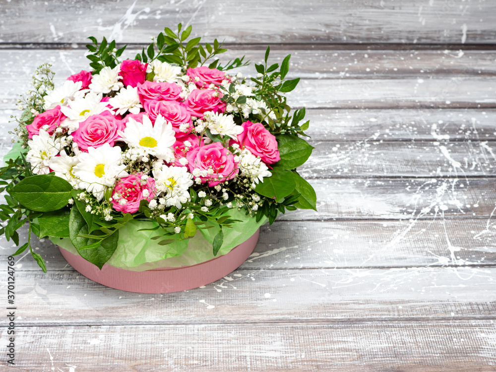 Naklejka premium Beautiful pink roses and white daisies in a box on a gray wooden background.
