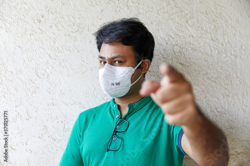 Adult man wearing KN95 respirator looking and pointing at camera