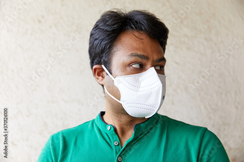 Middle aged South Asian adult male wearing a N95 Mask respirator and looking away, Left of camera. Profile shot- Anti-Pollution, Coronavirus, White Mask, Green Shirt, Chubby, Black Hair, Protective)