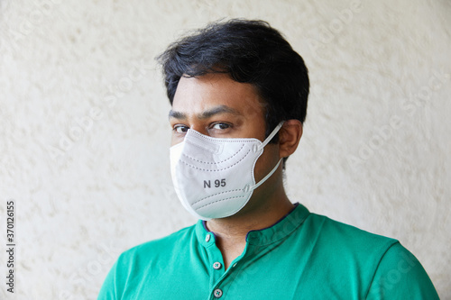 Adult Indian man wearing White N95 Mask in Green round neck T-shirt looking into the camera and looking into the camera with head faced 45 degrees