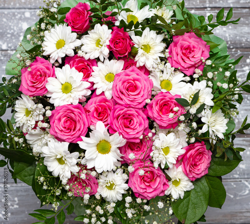 Beautiful pink roses and white daisies in a box on a gray wooden background. © Людмила Селянинова