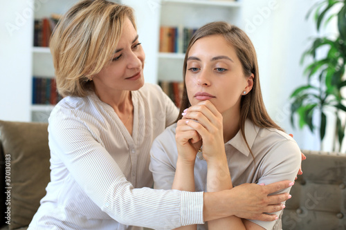 Concerned middle aged mother and adult daughter sit on couch having serious conversation  listen to her sharing problems.