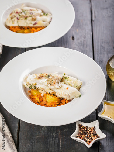 Two portions of halibut fillet baked with vegetables and potato confit garnish in a white plate. Restaurant recipes. Delicious natural seafood. Vertical shot