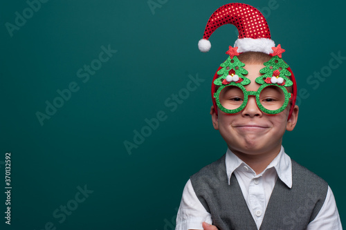 Portrait of happy little boy wearing headband with Santa Claus Hat and funny glasses with Christmas trees