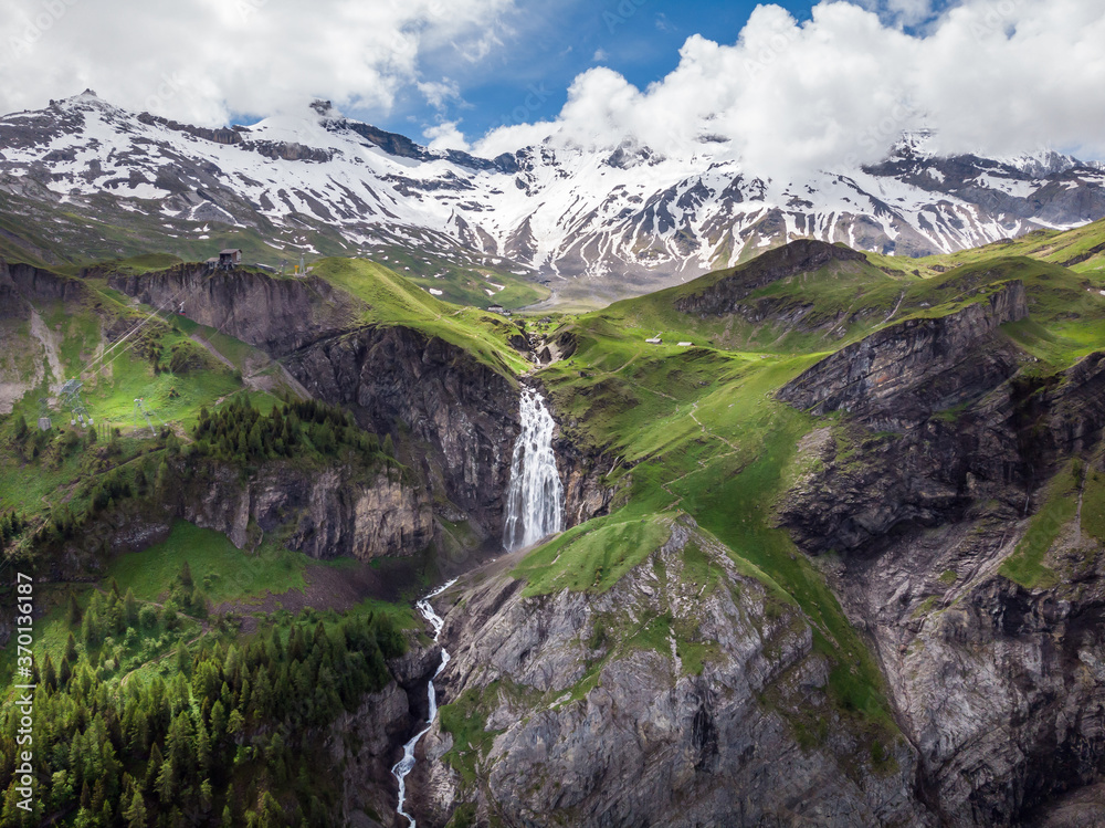 Stunning waterfall in the Swiss alps canton Berne. Aerial drone shot. Snowy mountains in the background.