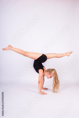 a young gymnast does an inverted splits on her hands on a white isolated background. Vertical orientation