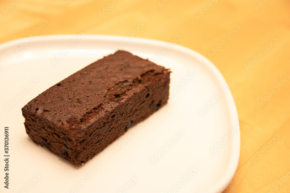 Delicious dark chocolate brownie on white plate with warm lighting at bakery shop.