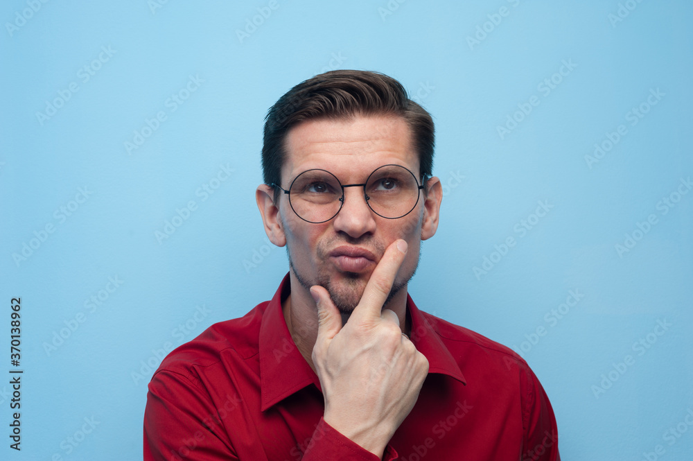 Portrait of a pensive serious young man in a shirt and glasses on a blue background. Portrait of a pensive serious young man in a shirt and glasses on a blue background.