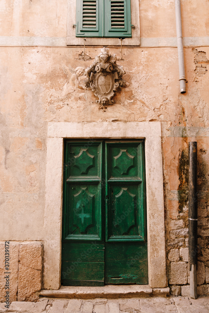 Closed double-leaf green wooden doors with patterns under the window and a carved figure in the wall.