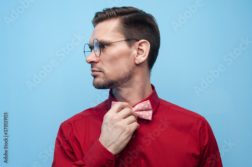 Fototapete Close-up of the hands of a young man in a red shirt correcting bow-tie against a blue background