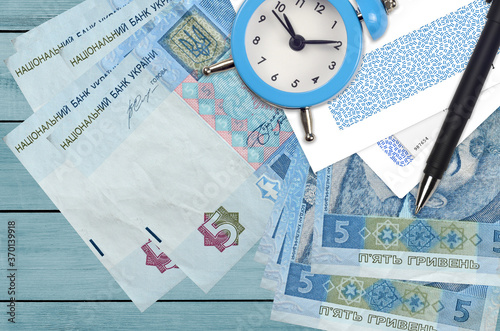 5 Ukrainian hryvnias bills and alarm clock with pen and envelopes. Tax season concept, payment deadline for credit or loan. Financial operations using postal service photo