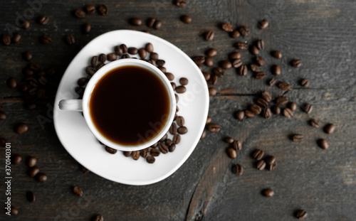 Coffee cup with roasted coffee beans on wooden table background. Mug of black coffe with scattered coffee beans on a wooden table. Fresh coffee beans.