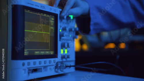 Photos Close up of hand turning dial of modern electronic oscilloscope