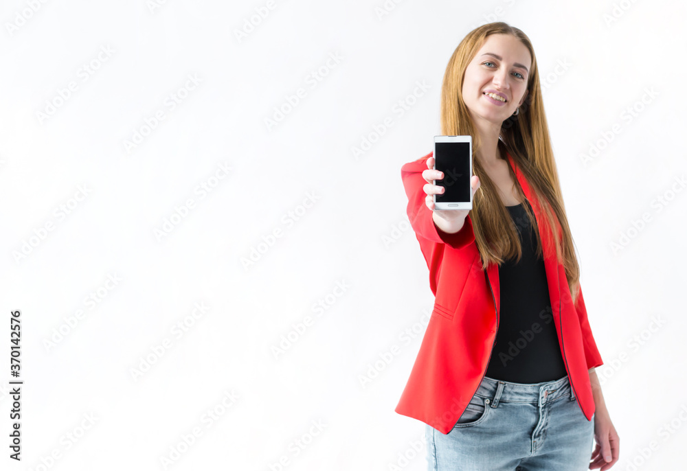 Portrait of a smiling girl who is standing with her hand outstretched forward holding a phone on a white background Portrait of a smiling girl who is standing with her hand outstretched forward holding a phone on a white background