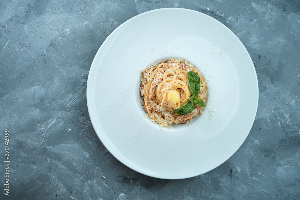 Italian pasta carbonara with yolk, bacon and parmesan cheese in a white plate on a gray background Italian pasta carbonara with yolk, bacon and parmesan cheese in a white plate on a gray background