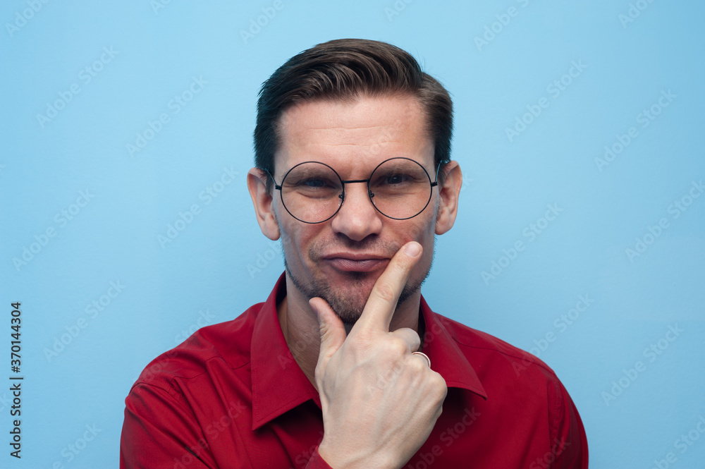 Portrait of a pensive serious young man in a shirt and glasses on a blue background. Portrait of a pensive serious young man in a shirt and glasses on a blue background.