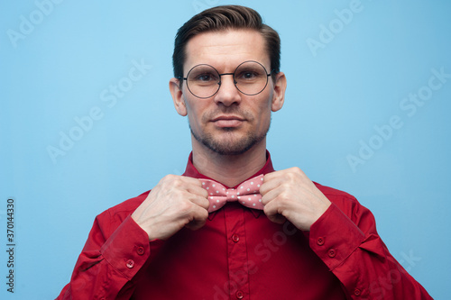 Fototapete Close-up of the hands of a young man in a red shirt correcting bow-tie against a blue background