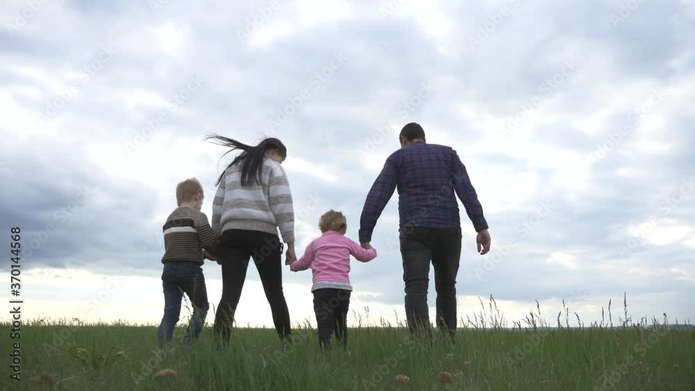 Young happy parents with children together, holding hands, walking on the green grass in the fresh air. A happy family has a fun weekend and socialize with each other. Young happy parents with children together, holding hands, walking on the green grass in the fresh air. A happy family has a fun weekend and socialize with each other.
