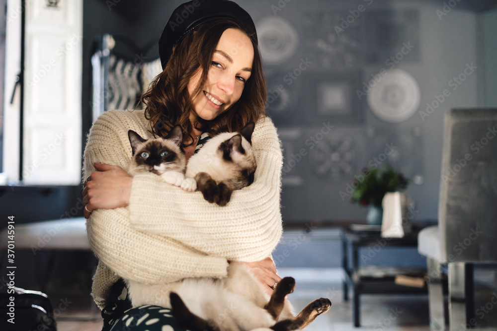 Attractive girl embracing her Siamese cats. Indoor portrait of cute woman playing with her two pets. Attractive girl embracing her Siamese cats. Indoor portrait of cute woman playing with her two pets.