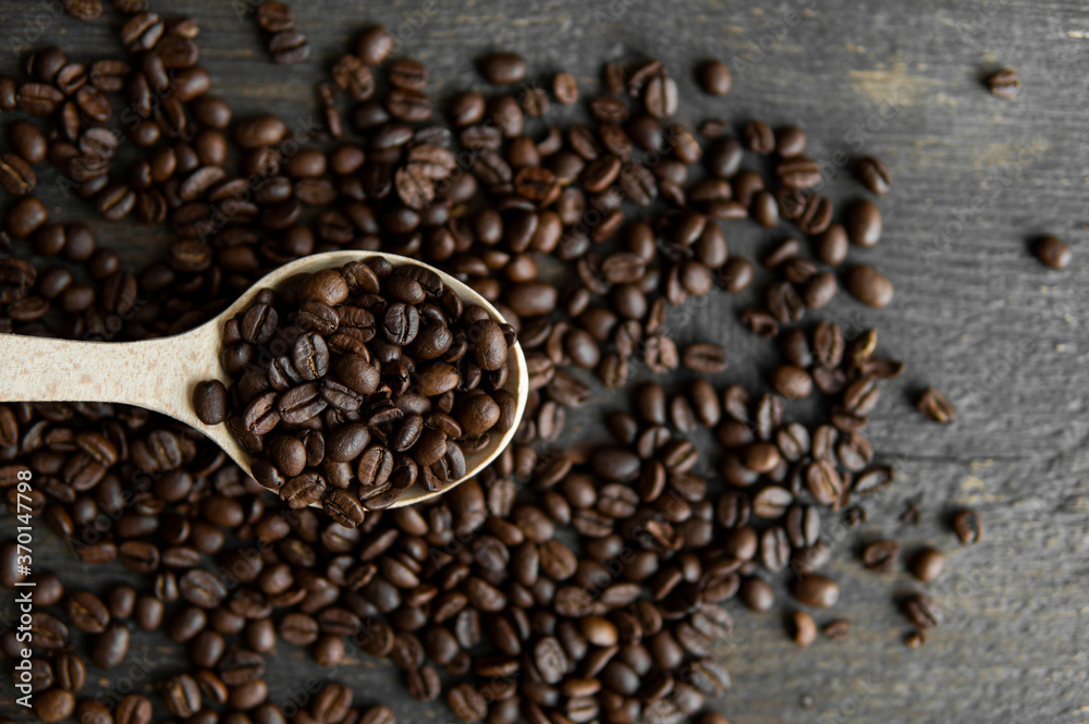 Fresh roasted arabica coffee beans in a wooden spoon and scattered coffee beans on a wooden table. Fresh roasted arabica coffee beans in a wooden spoon and scattered coffee beans on a wooden table.