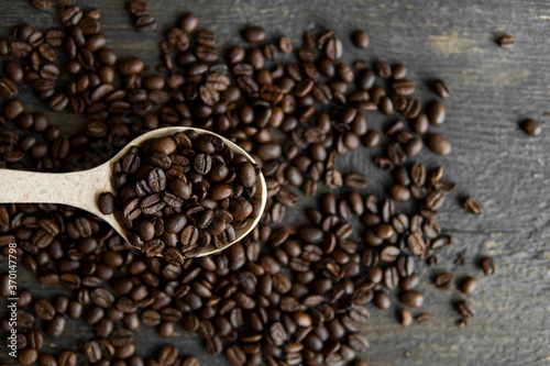 Fresh roasted arabica coffee beans in a wooden spoon and scattered coffee beans on a wooden table.