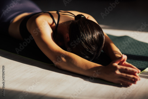 Beautiful sporty woman exercising at home, doing yoga for the spine on the floor, lying and resting after workout. 