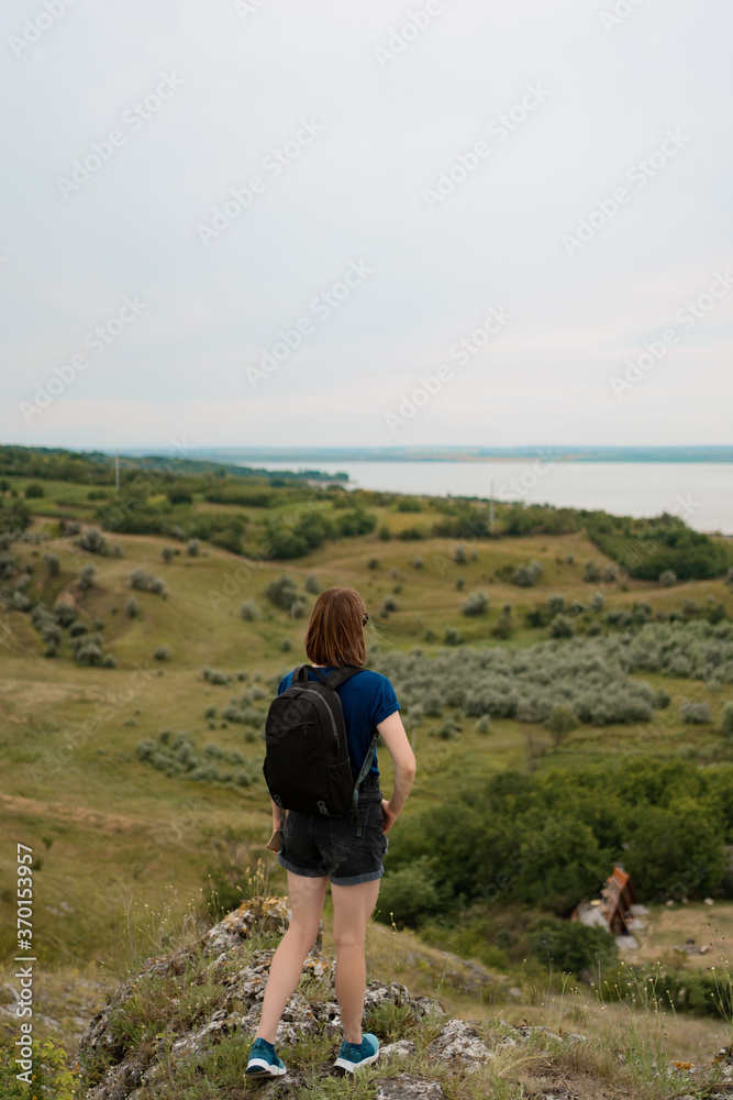 Young woman with backpack standing on cliff's edge and looking to the sky and beautiful nature. Discover wild places. Internal tourism