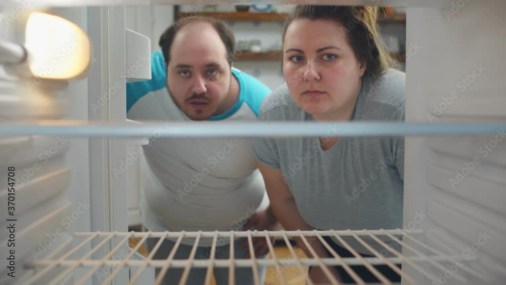 Overweight young couple on diet looking in empty fridge